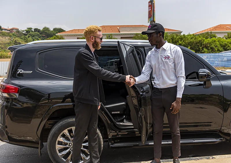 Motorista da Costa Phoebe a cumprimentar um cliente junto a uma Land Cruiser preta